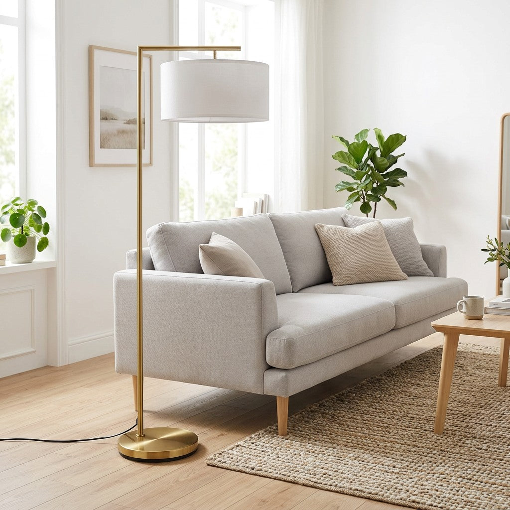 Guldgulvlampe med rund base ved sofa i lys stue hvor foden giver lampen et roligt tyngdepunkt