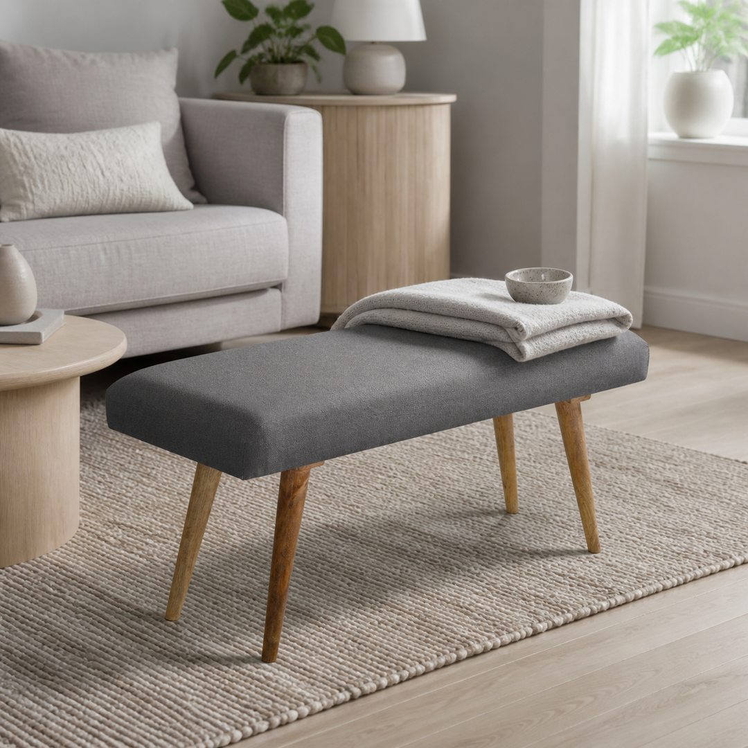 den grå polstrede bænk i lys grå stue med sofa, lyst træ, vævet uld og den polstrede bænk som materialemellemled