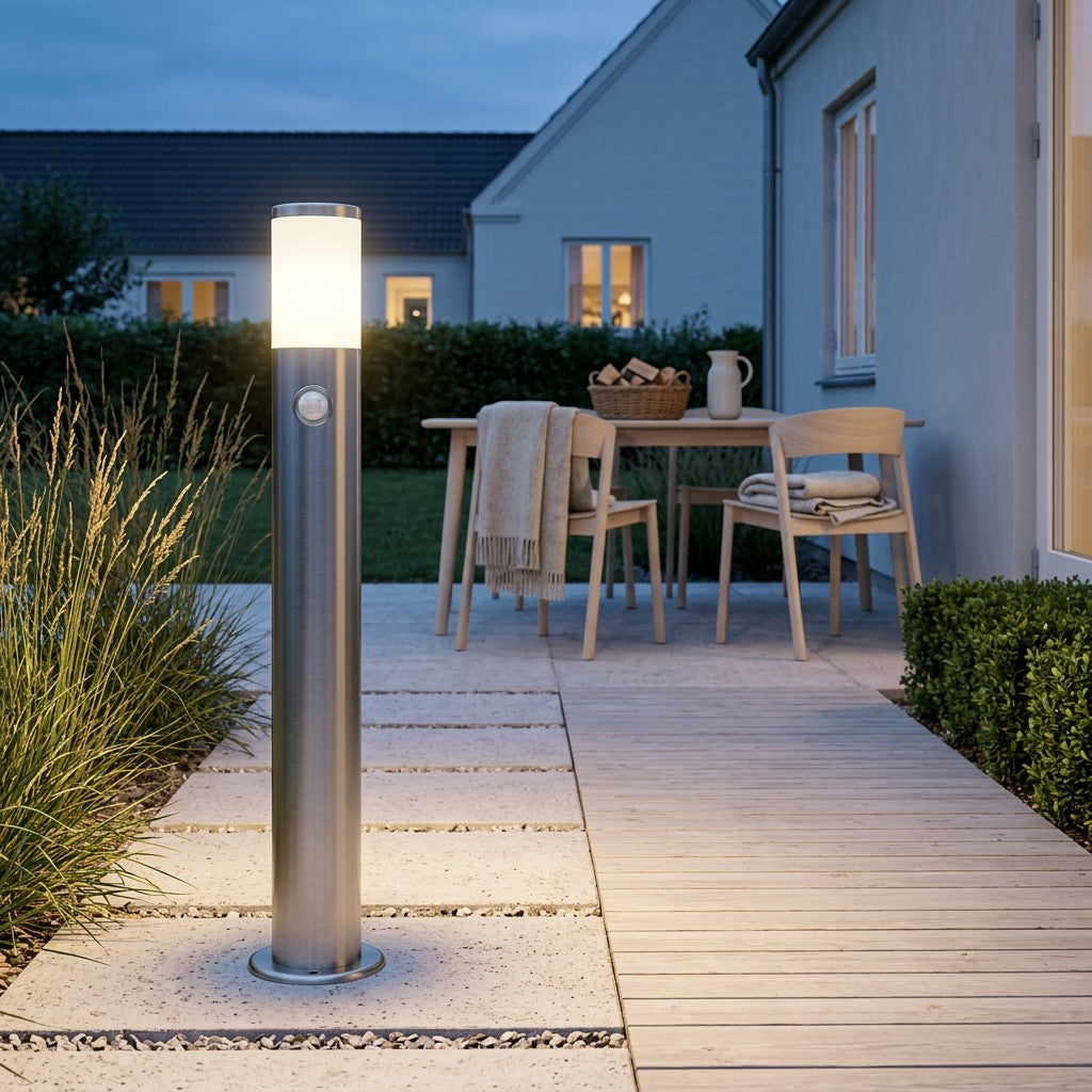 Udendørslampe i rustfrit stål langs en våd dansk havesti ved et træhus i det tidlige efterårsmørke