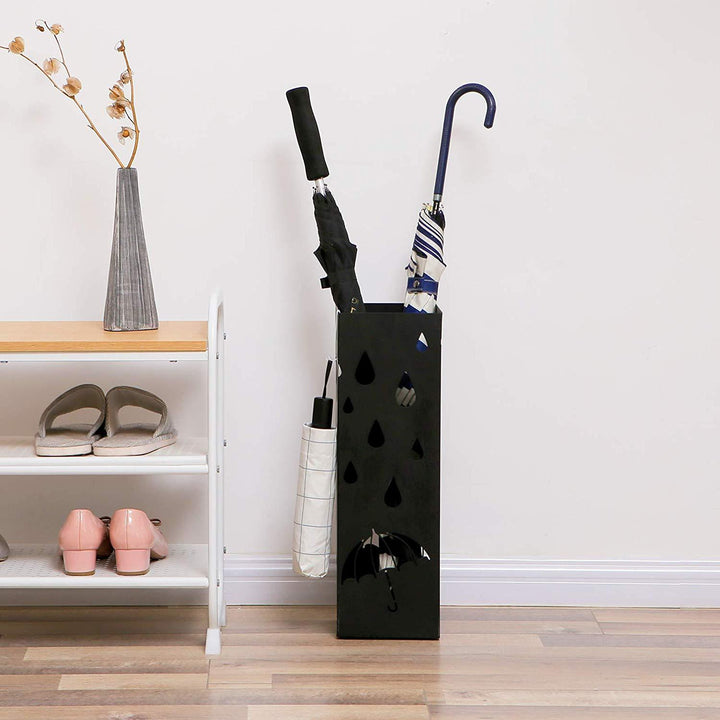 Paraplystativ i sort metal med grafiske udskæringer placeret i entré